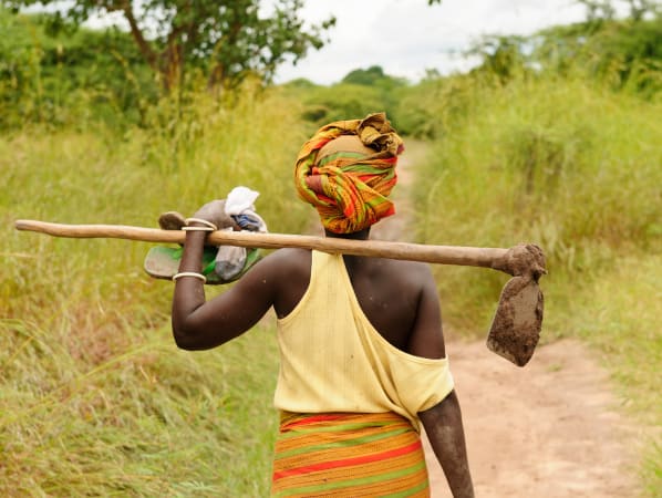 A woman from behind holding a shovel over her shoulder. 